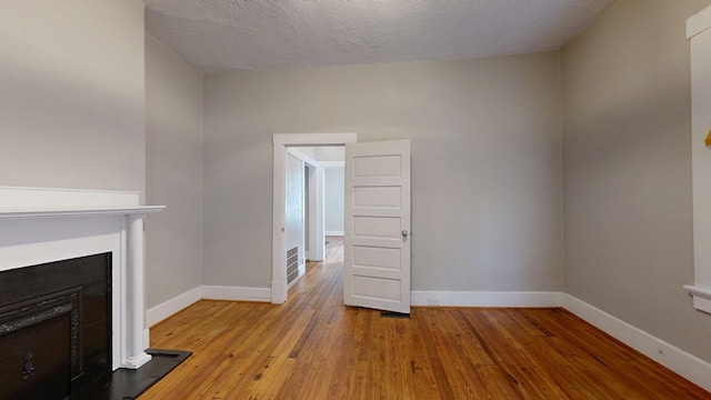 unfurnished living room with hardwood / wood-style flooring, baseboards, a fireplace, and a textured ceiling