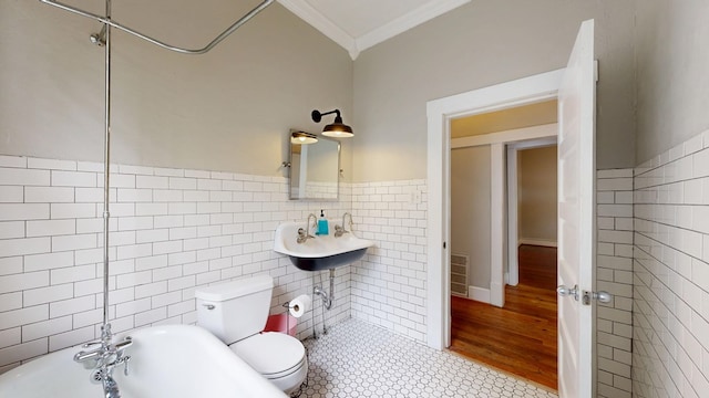 bathroom featuring tile walls, crown molding, toilet, a bathtub, and a sink