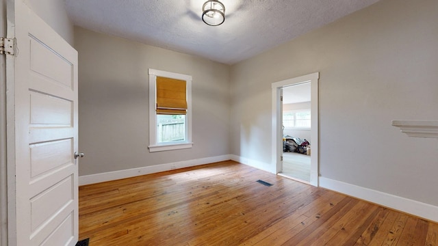 empty room with healthy amount of natural light, hardwood / wood-style flooring, baseboards, and a textured ceiling