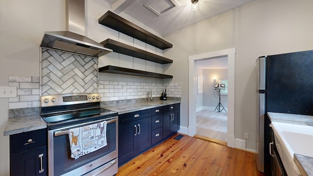 kitchen with stainless steel appliances, wall chimney range hood, blue cabinets, light wood-style flooring, and decorative backsplash