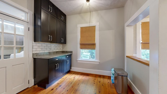 bar area with plenty of natural light, light wood-style flooring, baseboards, decorative backsplash, and a textured ceiling