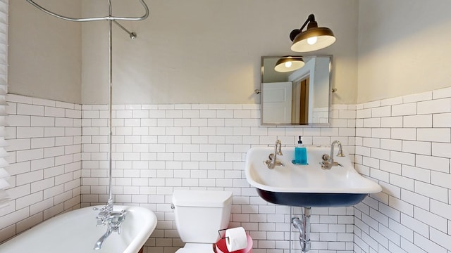 full bathroom with tile walls, toilet, a sink, and wainscoting