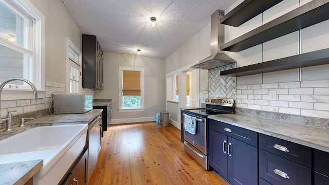 kitchen featuring stainless steel appliances, wall chimney range hood, open shelves, a sink, and blue cabinets