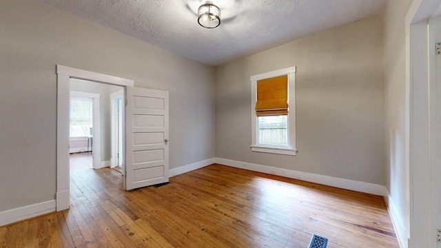 spare room featuring light wood finished floors, baseboards, and a textured ceiling