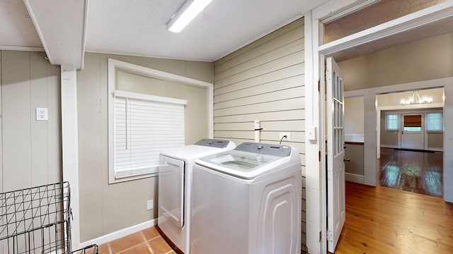 washroom featuring independent washer and dryer, a chandelier, light wood finished floors, wood walls, and baseboards
