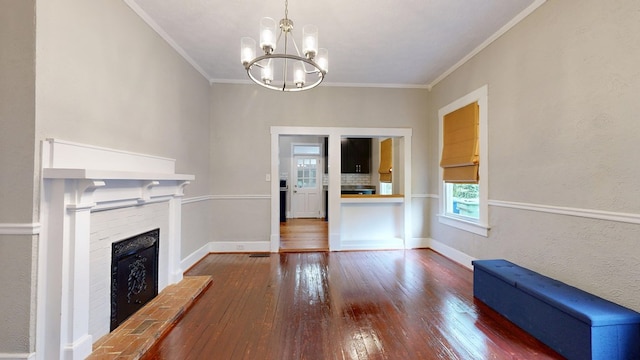 unfurnished living room featuring hardwood / wood-style flooring, ornamental molding, a chandelier, a fireplace with raised hearth, and baseboards
