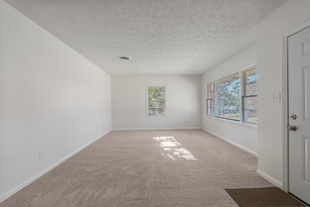 unfurnished room featuring light colored carpet, visible vents, a textured ceiling, and baseboards