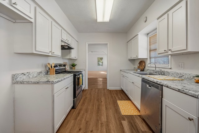 kitchen with under cabinet range hood, white cabinetry, appliances with stainless steel finishes, and a sink