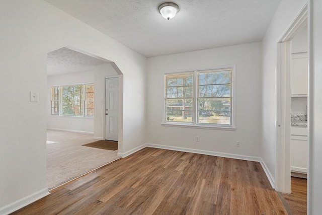 unfurnished room with baseboards, arched walkways, a textured ceiling, and wood finished floors