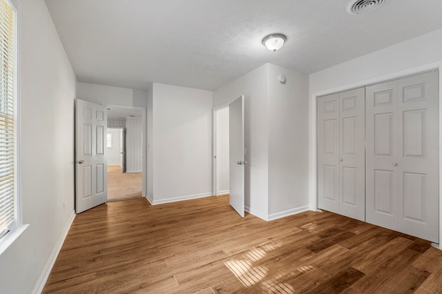 unfurnished bedroom featuring light wood finished floors, baseboards, visible vents, and a closet