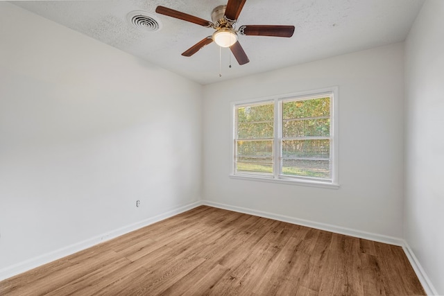 empty room with a textured ceiling, a ceiling fan, visible vents, baseboards, and light wood finished floors