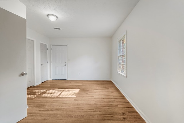 empty room featuring baseboards, visible vents, a textured ceiling, and light wood finished floors