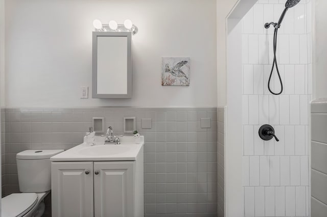 bathroom with tile walls, toilet, wainscoting, vanity, and tiled shower