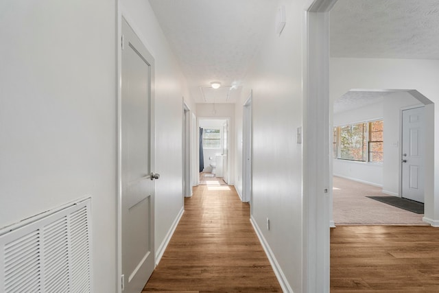 hall featuring visible vents, attic access, a textured ceiling, wood finished floors, and baseboards