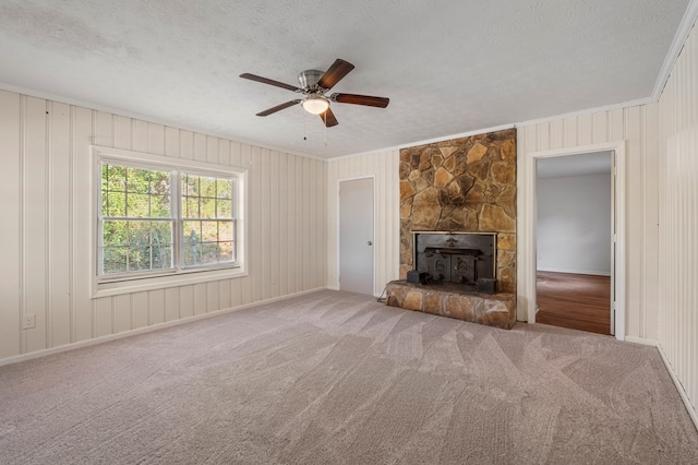 unfurnished living room featuring a textured ceiling, a stone fireplace, carpet, and crown molding