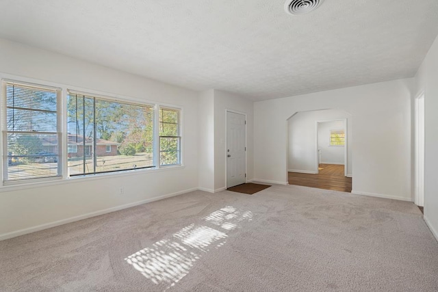 unfurnished bedroom featuring carpet floors, baseboards, visible vents, and arched walkways