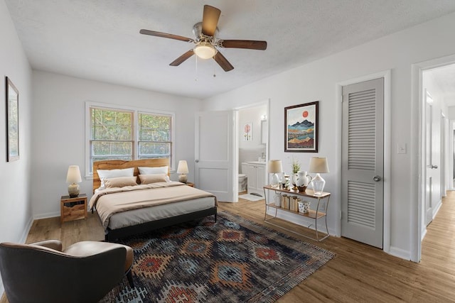 bedroom with ensuite bath, wood finished floors, and baseboards