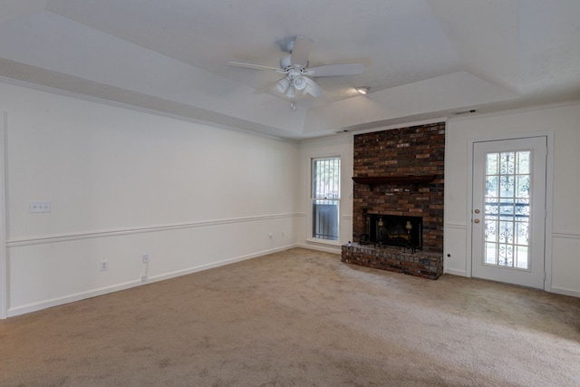 unfurnished living room with a brick fireplace, ceiling fan, light colored carpet, and a tray ceiling