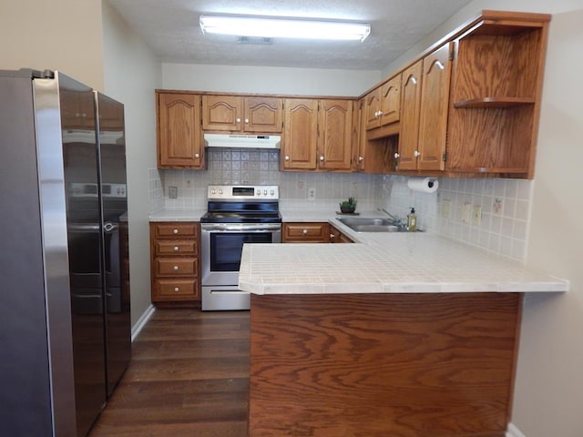 kitchen featuring dark wood-style floors, appliances with stainless steel finishes, a peninsula, under cabinet range hood, and a sink