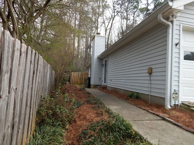 view of side of home featuring a garage, a chimney, and fence