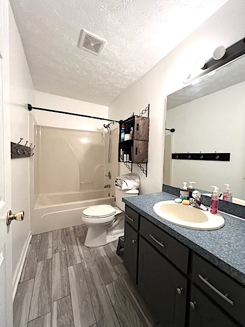 full bathroom with vanity, bathing tub / shower combination, toilet, a textured ceiling, and wood-type flooring