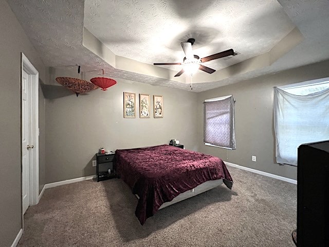 carpeted bedroom with ceiling fan, a textured ceiling, and a tray ceiling