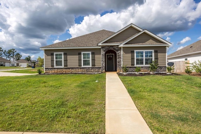 view of front of property featuring stone siding, roof with shingles, a front yard, and fence