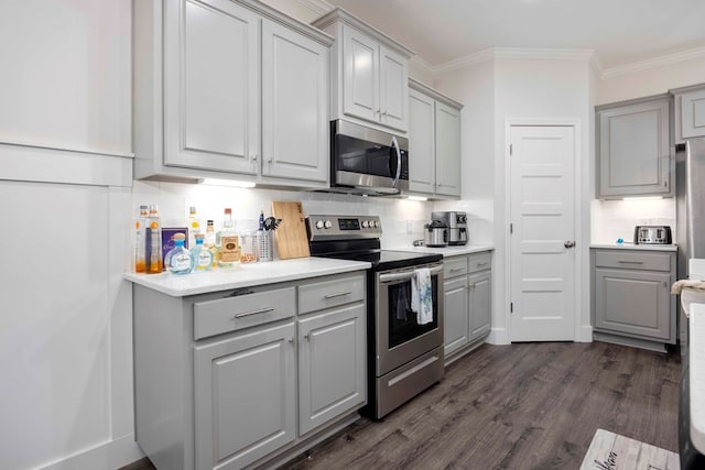 kitchen with gray cabinetry, stainless steel appliances, crown molding, and dark wood-type flooring