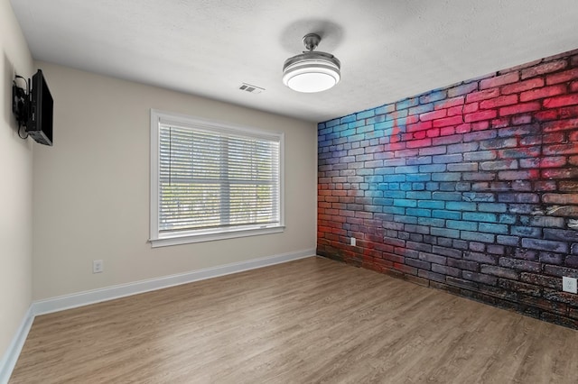 spare room featuring brick wall, a textured ceiling, and light hardwood / wood-style floors