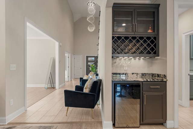 bar with wine cooler, dark brown cabinets, dark stone countertops, and light hardwood / wood-style floors