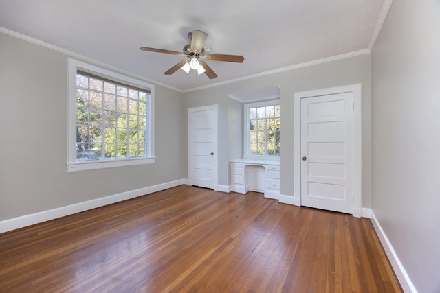 unfurnished bedroom with multiple windows, dark wood-type flooring, built in desk, and ornamental molding