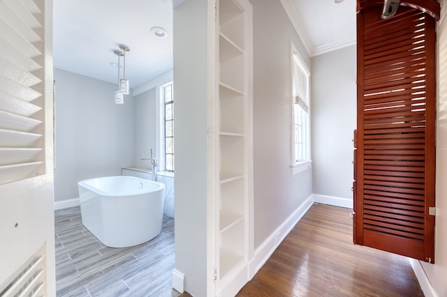 interior space with a bathing tub, ornamental molding, and hardwood / wood-style floors