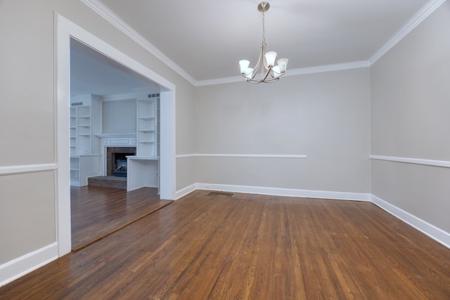 unfurnished room featuring a fireplace, a notable chandelier, crown molding, dark wood-type flooring, and built in shelves