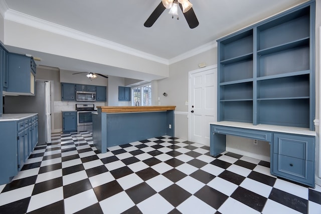 kitchen with appliances with stainless steel finishes, built in desk, ornamental molding, ceiling fan, and blue cabinetry