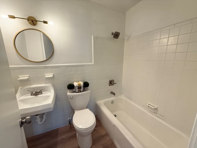 bathroom with toilet, a wainscoted wall, wood finished floors, a sink, and tile walls