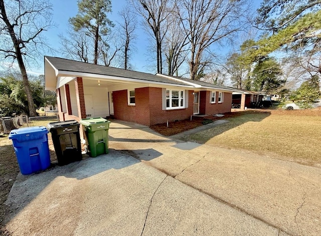 single story home with an attached carport, concrete driveway, brick siding, and fence