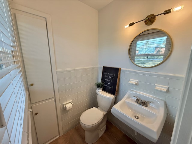 half bath featuring toilet, a wainscoted wall, a sink, wood finished floors, and tile walls