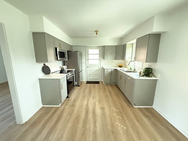 kitchen with stainless steel appliances, a sink, light countertops, light wood-type flooring, and gray cabinets