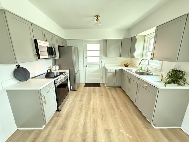 kitchen featuring appliances with stainless steel finishes, light wood-style floors, a sink, and gray cabinetry