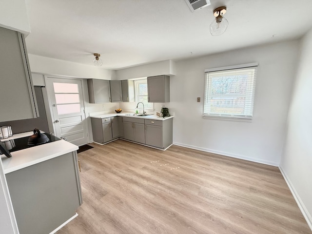 kitchen with light countertops, gray cabinetry, light wood-style floors, a sink, and baseboards