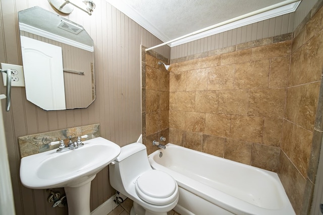 bathroom with tiled shower / bath combo, toilet, crown molding, and wood walls