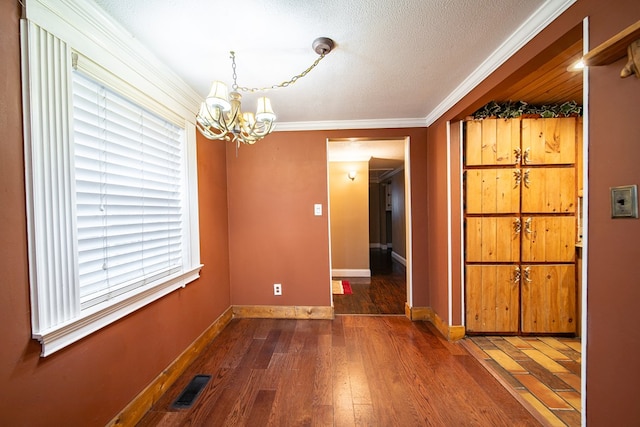 unfurnished dining area featuring crown molding, dark hardwood / wood-style flooring, a chandelier, and a textured ceiling