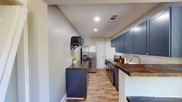 kitchen with blue cabinets, light hardwood / wood-style flooring, appliances with stainless steel finishes, tasteful backsplash, and butcher block counters