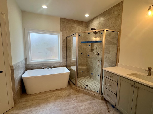 bathroom featuring independent shower and bath, vanity, and tile walls