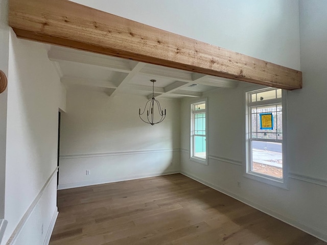 empty room with beam ceiling, a notable chandelier, coffered ceiling, and hardwood / wood-style floors