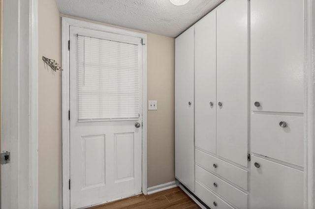 doorway to outside featuring dark wood-type flooring, baseboards, and a textured ceiling