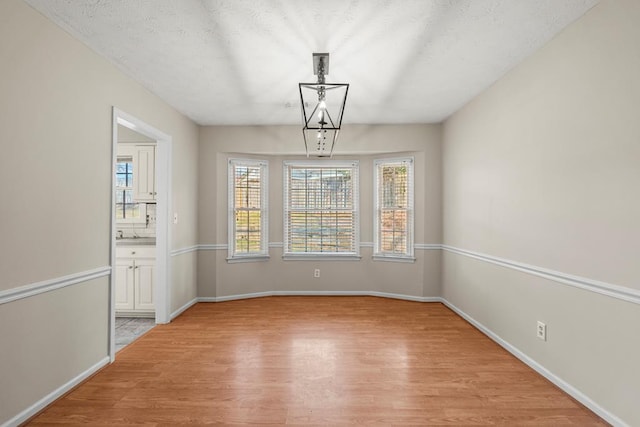 unfurnished dining area featuring light wood finished floors, a textured ceiling, and baseboards