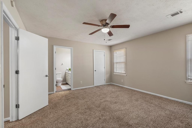 unfurnished bedroom featuring visible vents, a textured ceiling, ensuite bath, carpet, and baseboards