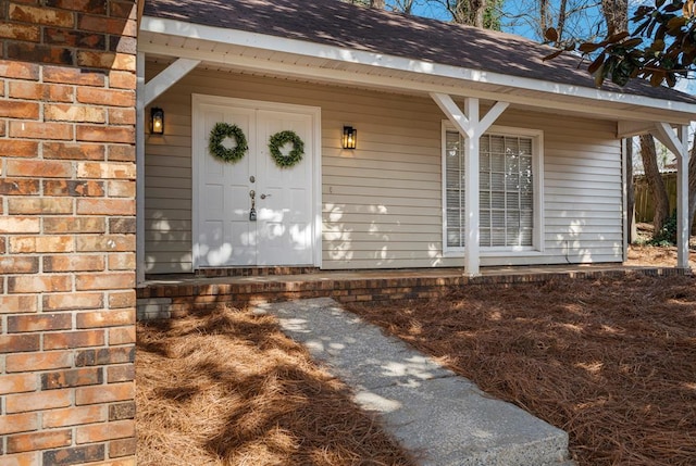 property entrance with brick siding, roof with shingles, and covered porch