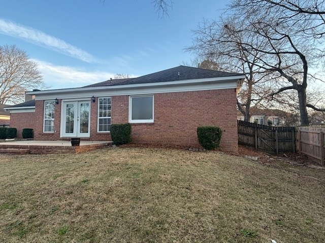 back of house with french doors, a fenced backyard, a lawn, and brick siding